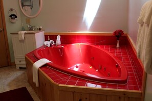 Una vasca da bagno rossa in un bagno con una panca di legno, un asciugamano bianco e un piccolo vaso con fiori.