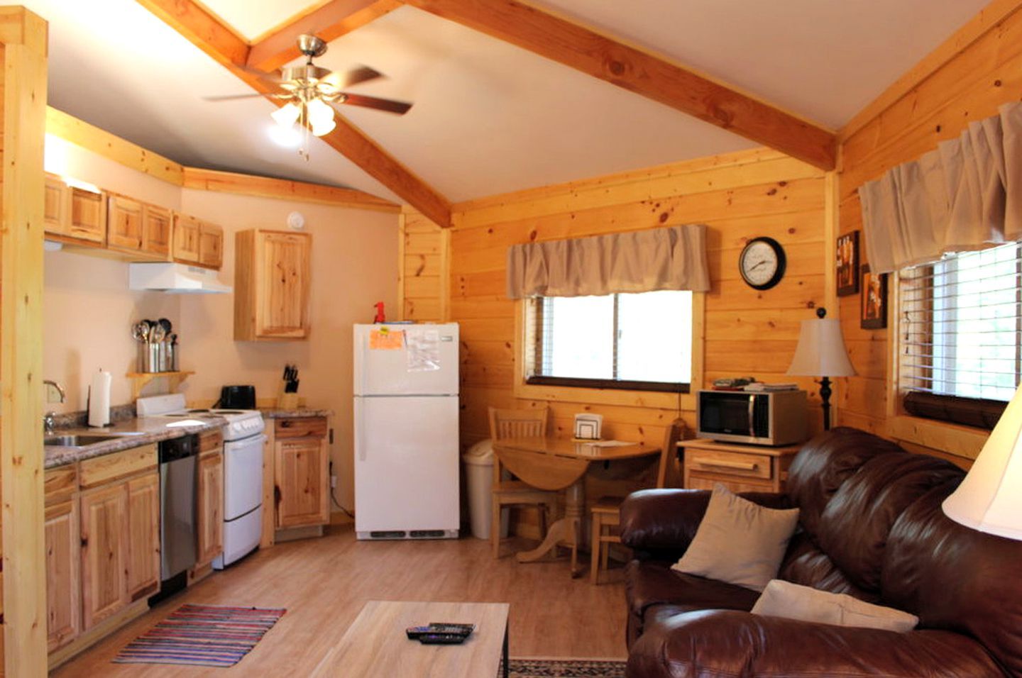 Een gezellig interieur van een chalet met houten wanden, een keuken met houten kastjes, een eethoek en een leren bank.