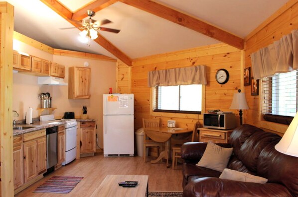 A cozy cabin interior with wooden walls, a kitchen with wooden cabinets, a dining area, and a leather couch.