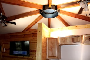 Een houten plafond met zichtbare balken, een plafondventilator en een televisie.