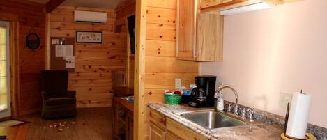 Ambiente in legno con angolo cottura, dotato di lavello, macchina per caffè e pensili.