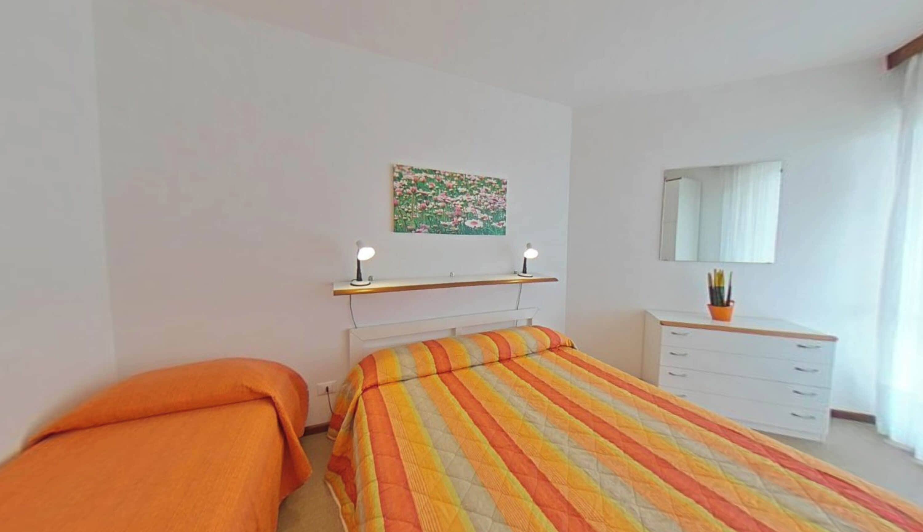 A bedroom with a bed, a desk, a dresser, a mirror, and a painting on the wall.
