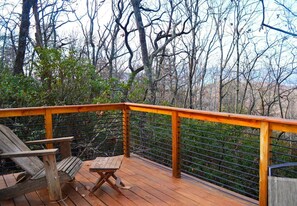 Una terraza de madera con baranda metálica, una silla de madera y una mesita.