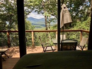 Een houten terras met een bed, twee stoelen en een tafel.