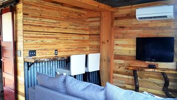 A cozy cabin interior with a wooden wall, a sofa, a television, and an air conditioning unit.