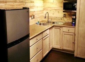 A compact kitchen with wooden cabinets, a stainless steel sink, a microwave, and a refrigerator.