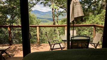 A wooden deck with a bed, two chairs, and a table.
