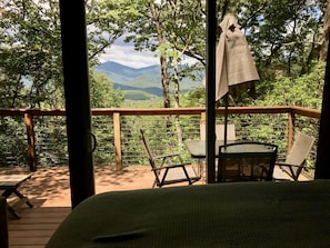 A wooden deck with a bed, two chairs, and a table.