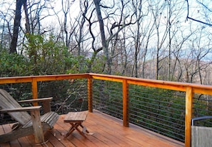 Una terraza de madera con baranda metálica, una silla de madera y una mesita.