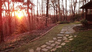 A stone pathway leading through a wooded area with a building on the right.