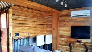 Et hyggeligt sommerhusinteriør med trævæg, sofa, fjernsyn og en aircondition.
