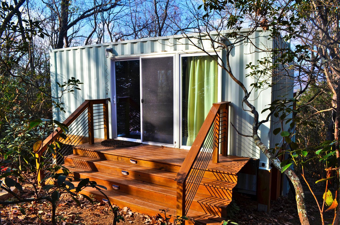 A small cabin with a wooden deck, a sliding glass door, and a staircase.