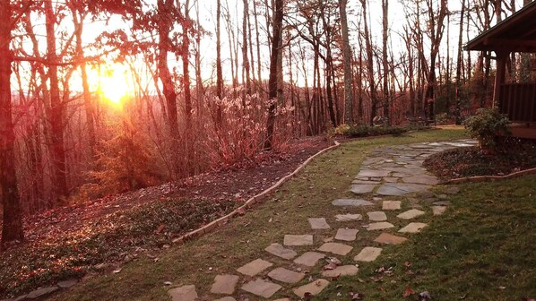 A stone pathway leading through a wooded area with a building on the right.