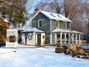 Ein zweistöckiges Haus mit Veranda, einem kleinen Anbau und einem schnee bedeckten Vorgarten.