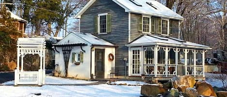 Une maison à deux étages avec un porche, une petite dépendance attenante et une cour enneigée.