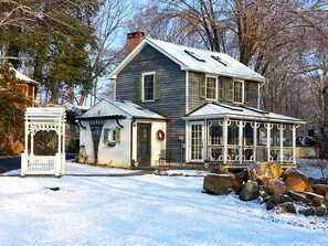 A two-story house with a porch, a small attached structure, and a snow-covered yard.
