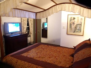 Ein Schlafzimmer mit Bett, Kommode, Fernseher und einem Bild an der Wand.