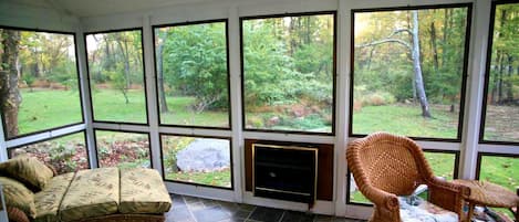 A sunroom with large windows, a fireplace, a sofa, and a chair.