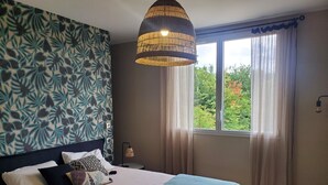 A bedroom with a bed, a window with curtains, a wall with a leaf pattern, and a hanging light fixture.