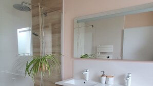 A modern bathroom with a shower, two sinks, a mirror, and wooden cabinetry.