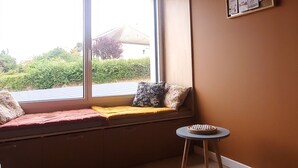A room with a large window, a small stool, and a bench with cushions.