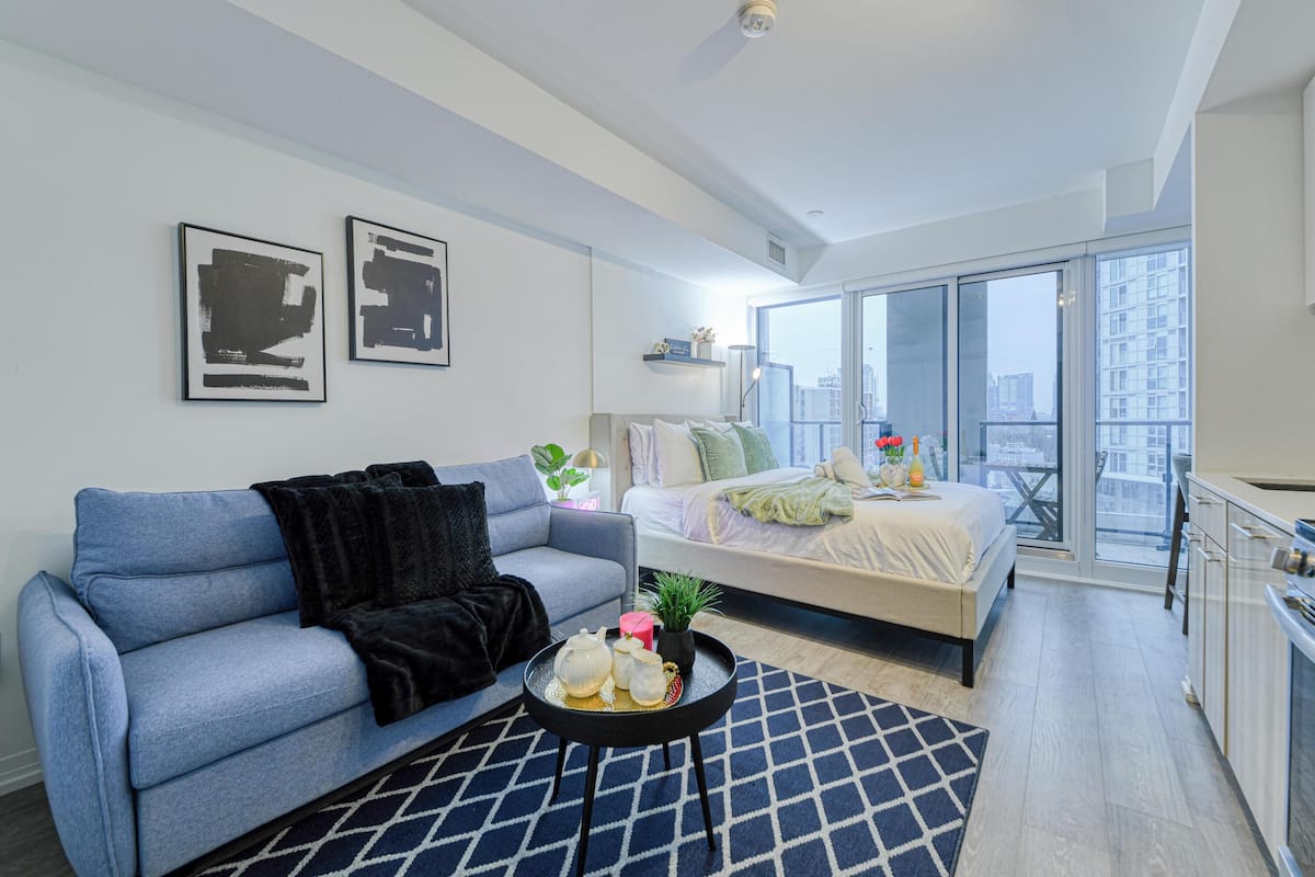 Un appartement moderne doté d’un canapé, d’un lit, d’un coin repas et de grandes fenêtres offrant une vue sur la ville.