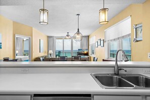 A modern kitchen with a large island, a dining area with a view, and a balcony with a view. - Summerwind Center 504 (Navarre)