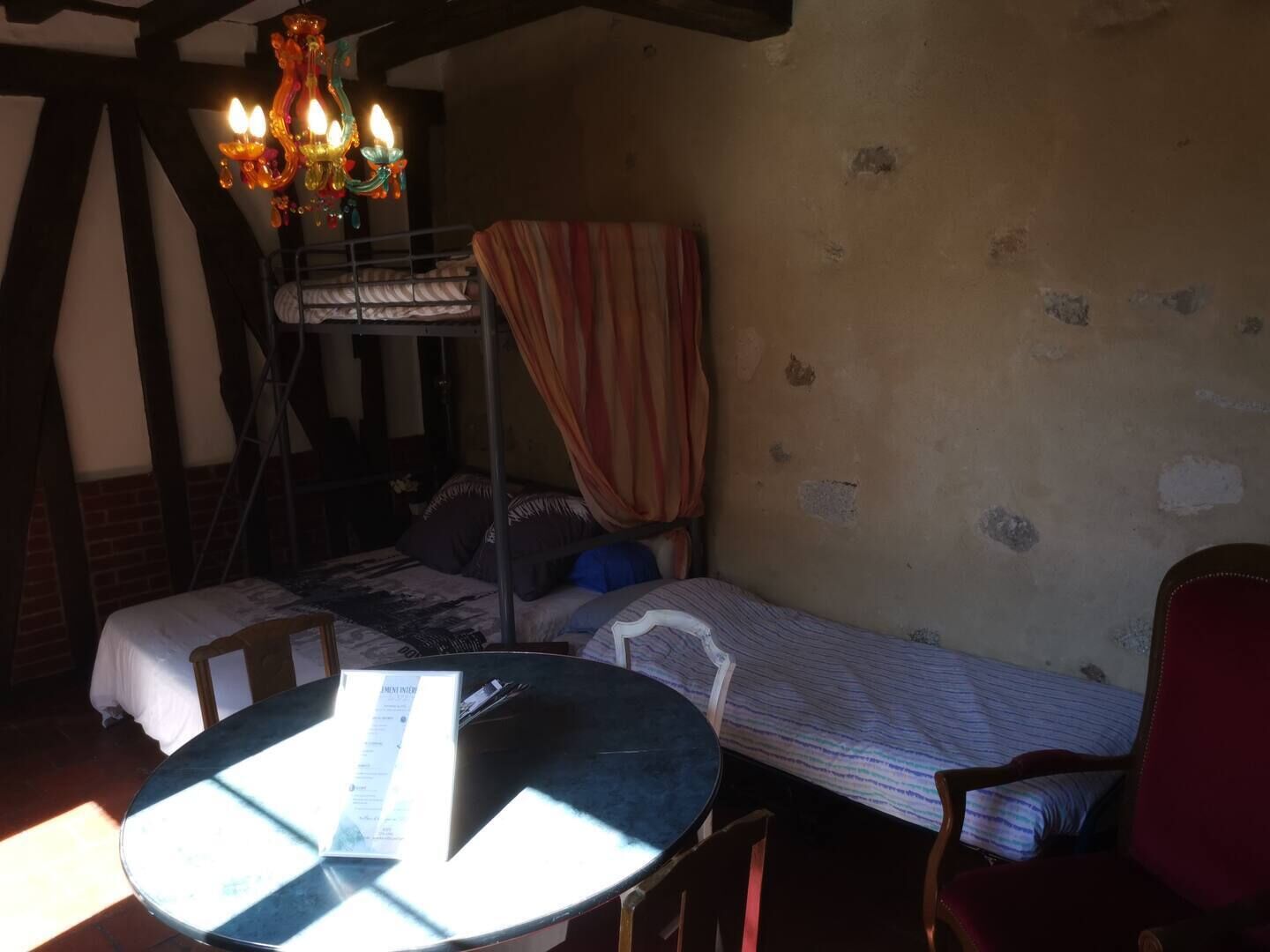 Une chambre avec un lit superposé, une table ronde sur laquelle est posé un menu, et un lustre.