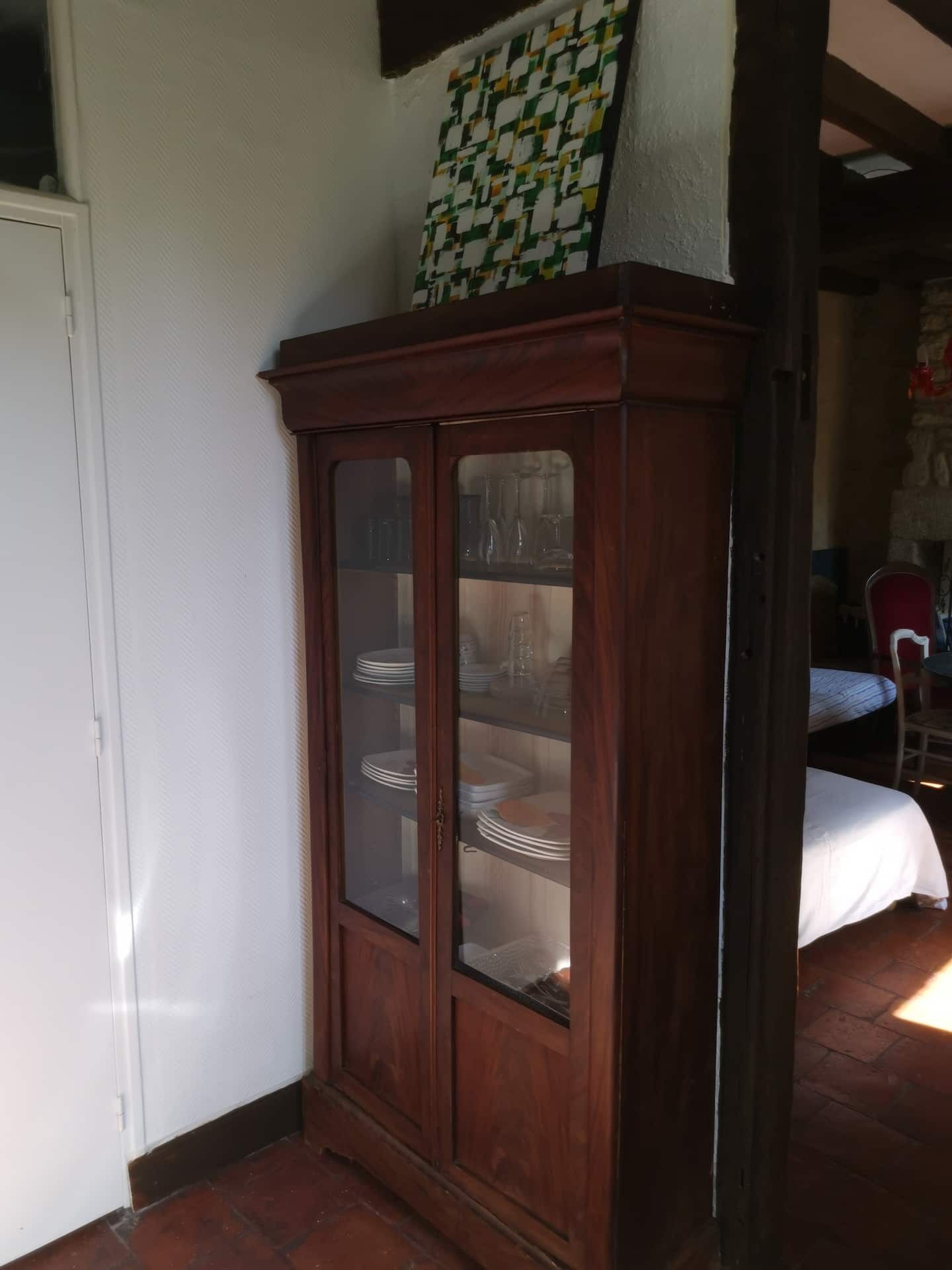 Un armario de madera con puertas de cristal que contiene platos y vasos, una puerta blanca y un patrón de pared a cuadros.