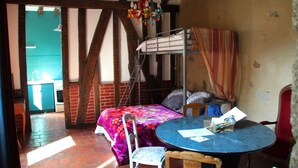 Una habitación con literas, una mesa redonda con sillas, una lámpara colgante y vistas a una cocina a través de una puerta abierta.