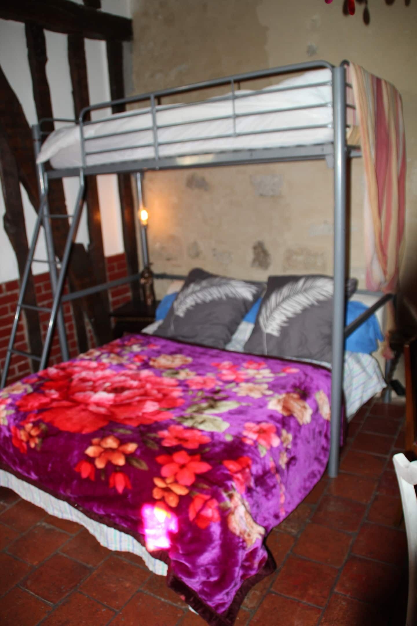 Una cama litera con cubrecama floral, una escalera y una pared con diseño de ladrillo.