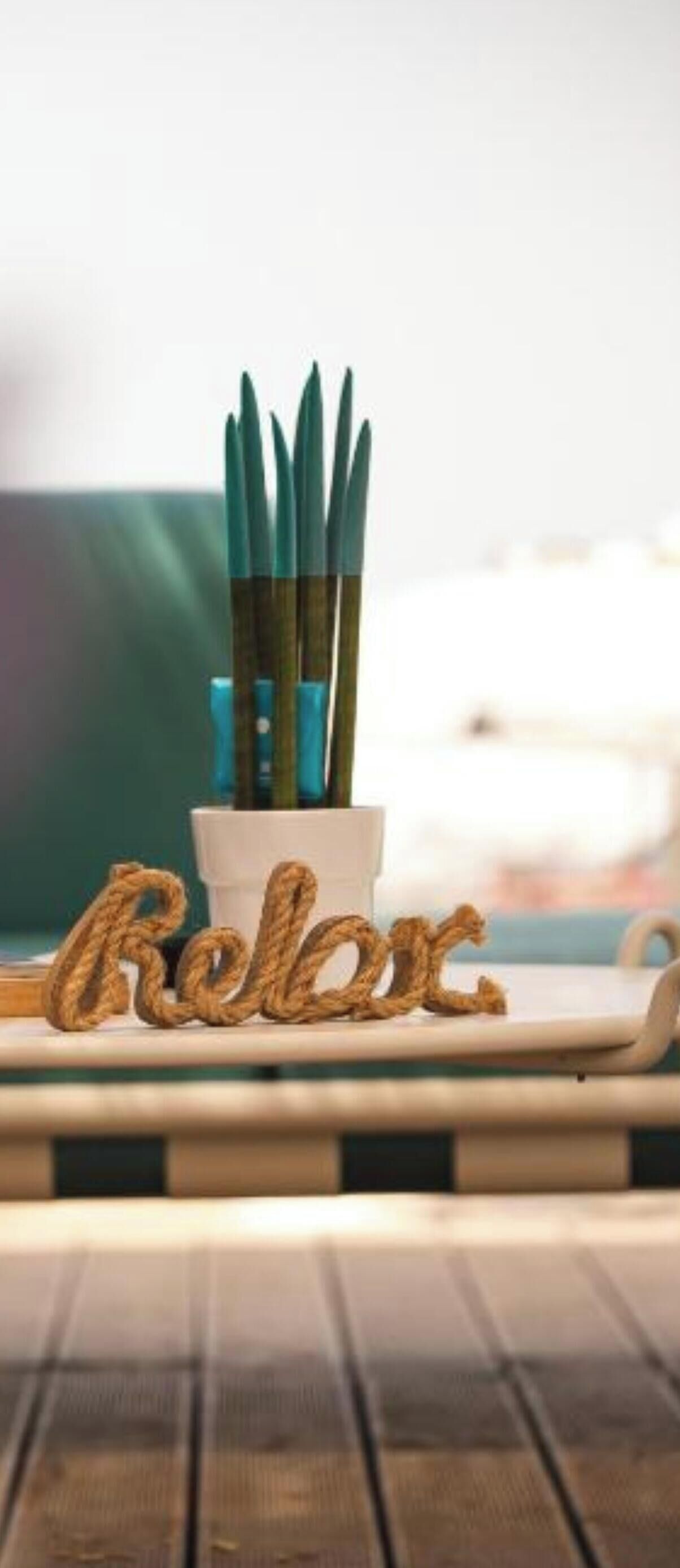 A wooden table with a white cup and green chopsticks in a holder, and a decorative sign spelling 'Relax.'