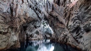 A cave interior with natural rock formations and a reflective water pool. - Royal Rooms (Laura)