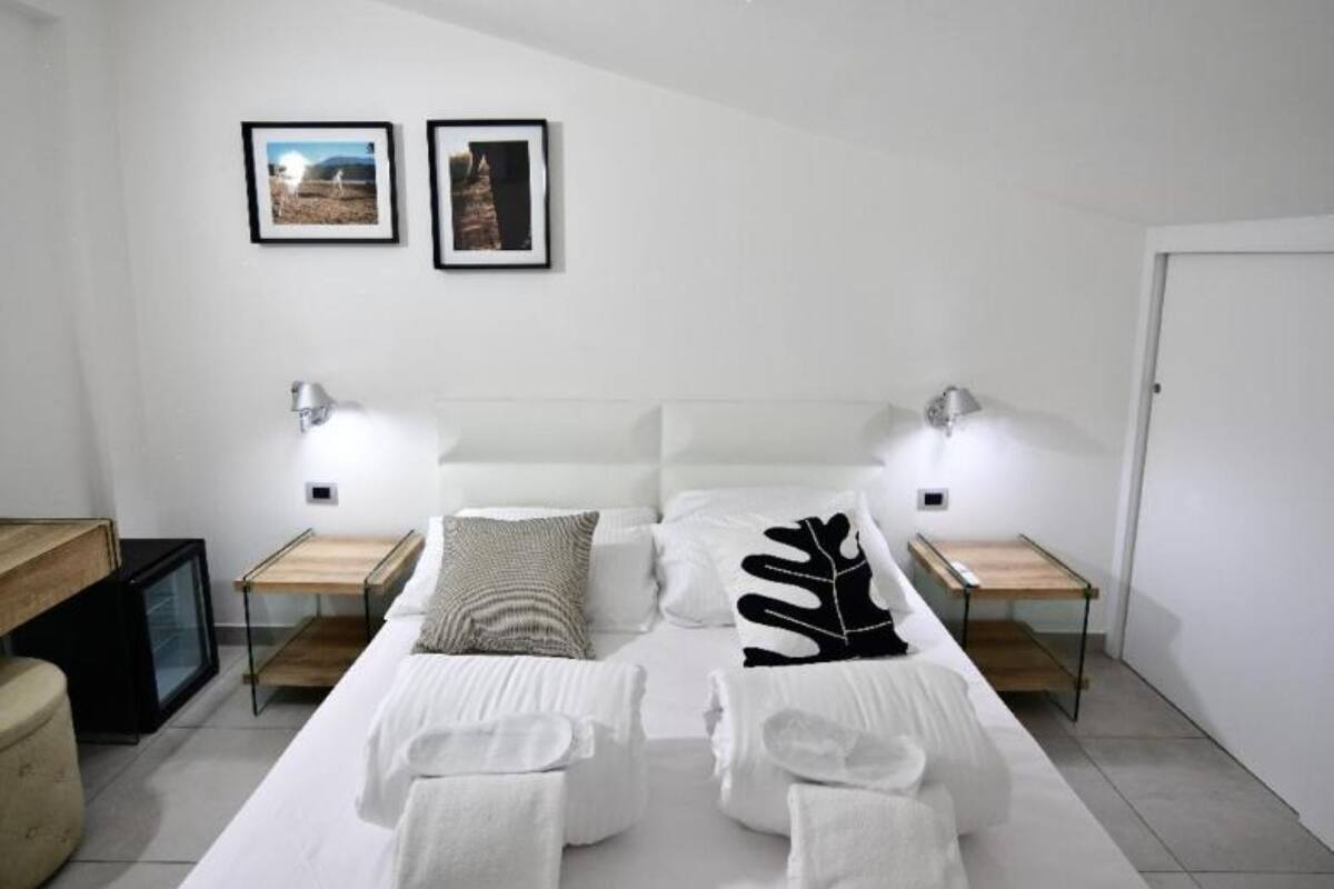 Un lit bien fait, avec des serviettes, une tête de lit, des lampes de chevet et deux tableaux encadrés accrochés au mur.