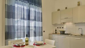 A modern kitchen with white cabinets, a gas stove, and a dining area with a table set for two. - Royal Rooms (Laura)