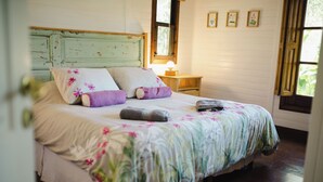 A bed with floral bedding, a nightstand with a lamp, and a window with a view. - Cabaña Los Juncos (Tigre)