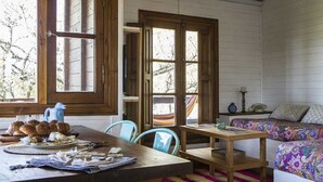 A rustic room with a wooden table, chairs, a bed with colorful bedding, and a window with a view of trees. - Cabaña Los Juncos (Tigre)
