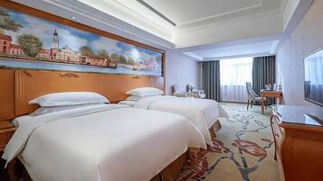 Quarto de hotel com duas camas, televisão, escrivaninha e um quadro na parede.