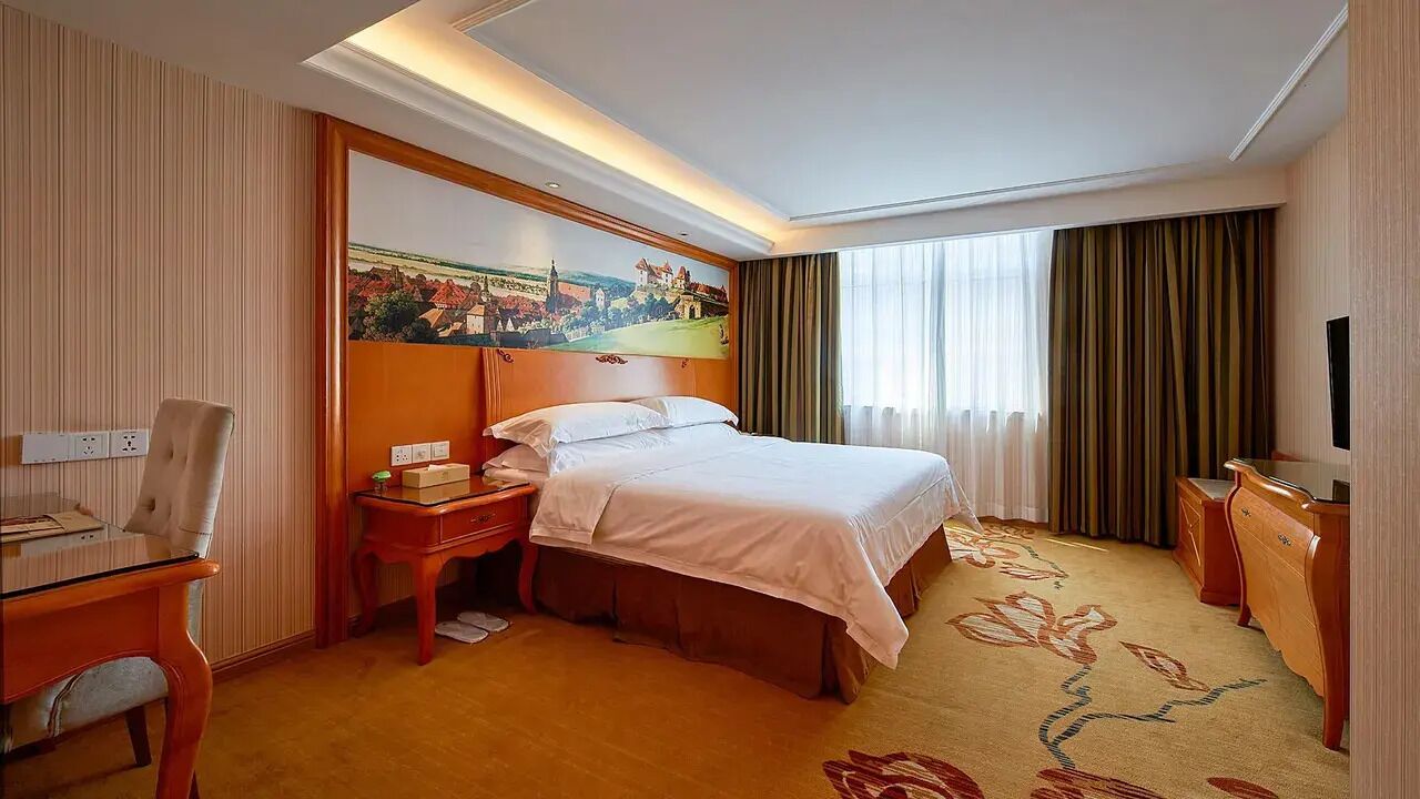 Habitación de hotel con cama, escritorio, silla, mesita de noche, televisión y un cuadro en la pared.
