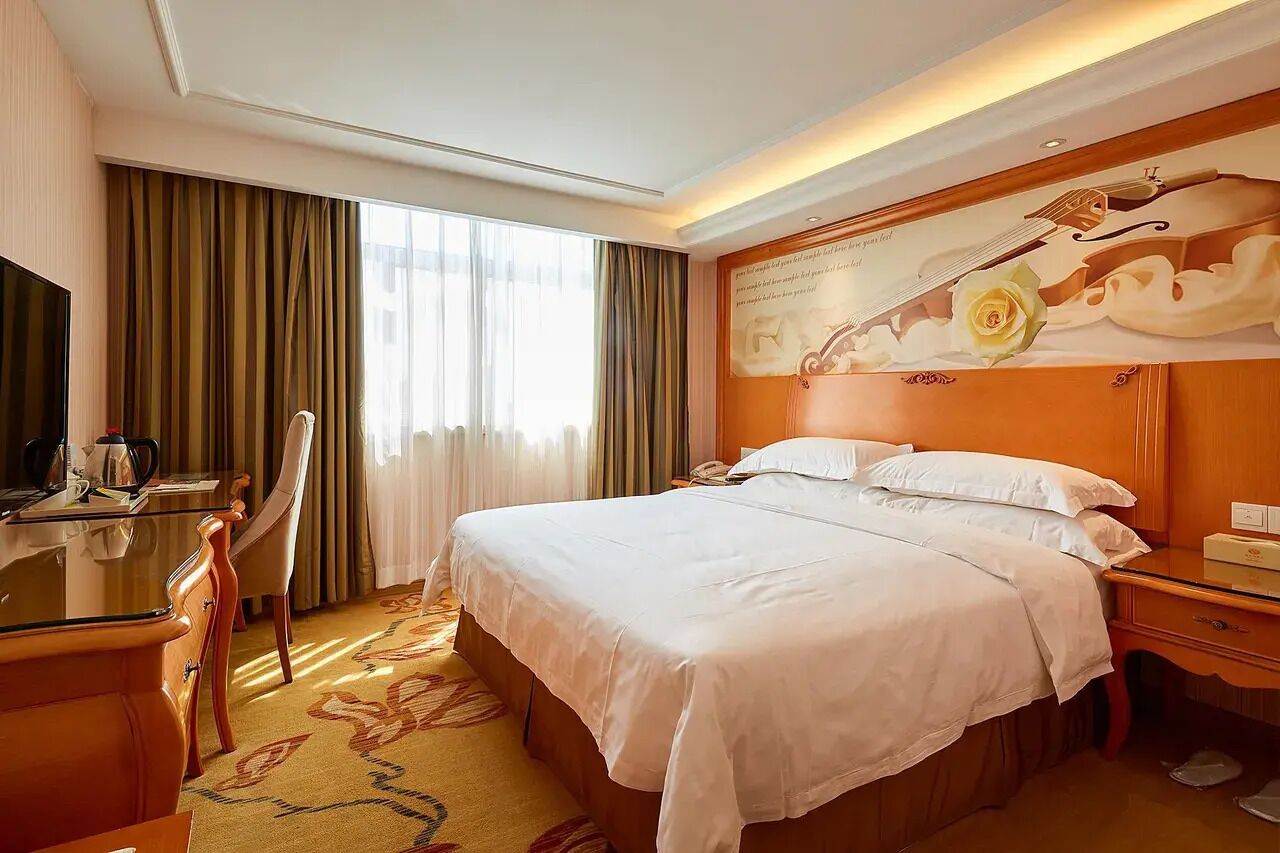 A hotel room with a bed, a desk, a chair, and a television.