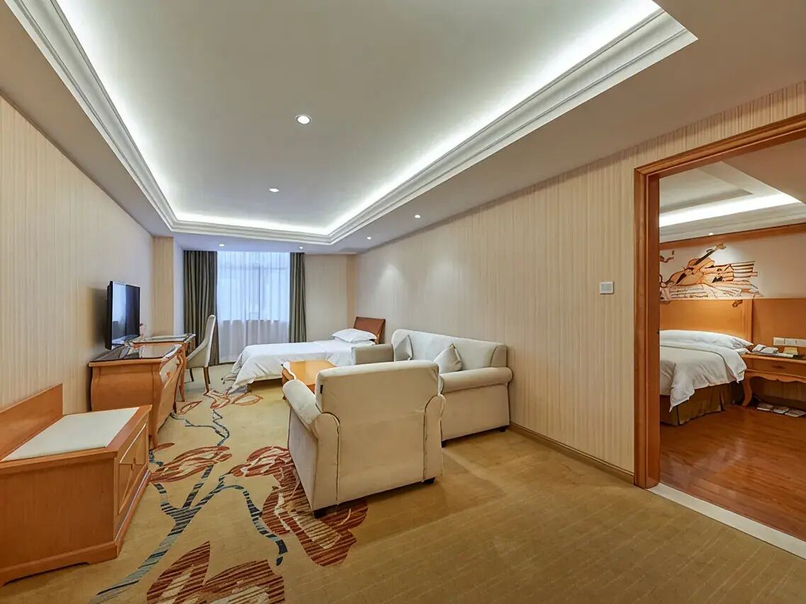 Ein Hotelzimmer mit einem Bett, einem Schreibtisch, einem Sessel, einem Fernseher und Teppichboden.