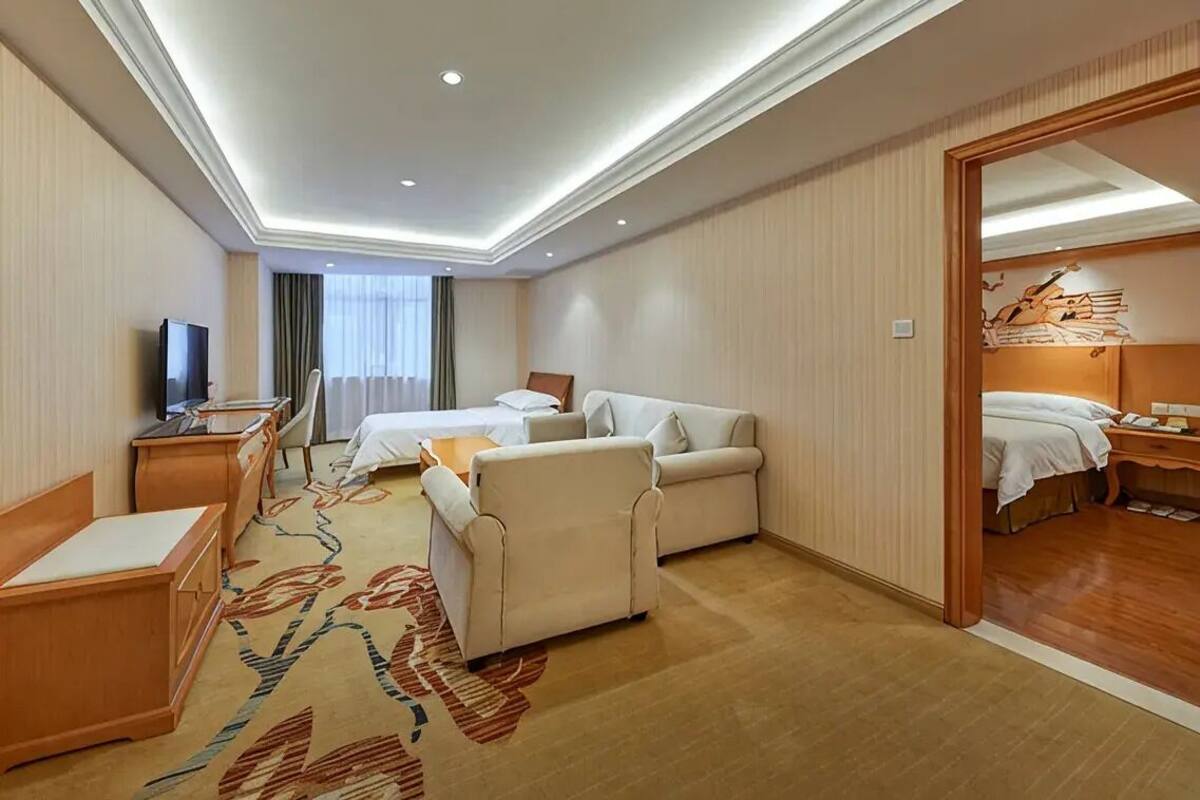 A hotel room with a bed, a desk, a chair, a television, and a carpeted floor.