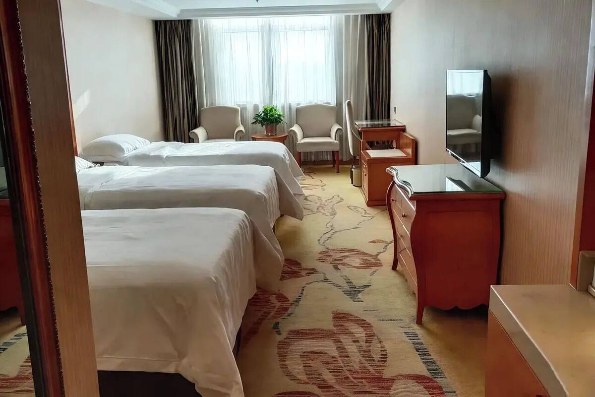 A hotel room with two beds, a desk, a chair, a TV, and a window with curtains.