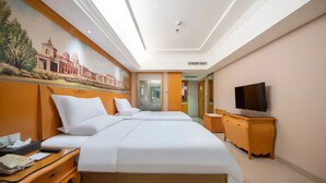 Ein Hotelzimmer mit zwei Betten, einem Schreibtisch, einem Fernseher und einem Wandgemälde.