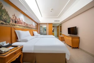 Ein Hotelzimmer mit zwei Betten, einem Schreibtisch, einem Fernseher und einem Wandgemälde.