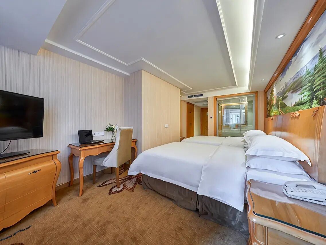 Ein Hotelzimmer mit einem Bett, einem Schreibtisch mit Computer, einem Fernseher und einem Bild an der Wand.