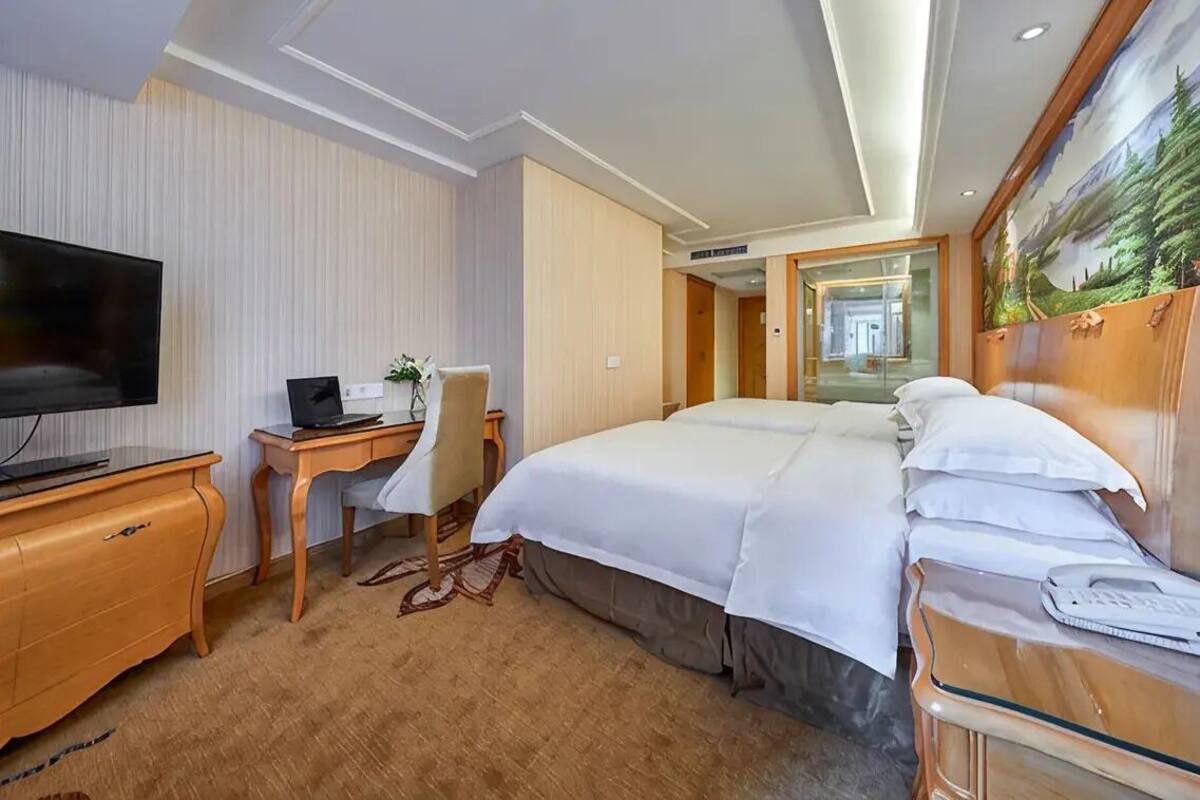 A hotel room with a bed, a desk with a computer, a television, and a painting on the wall.