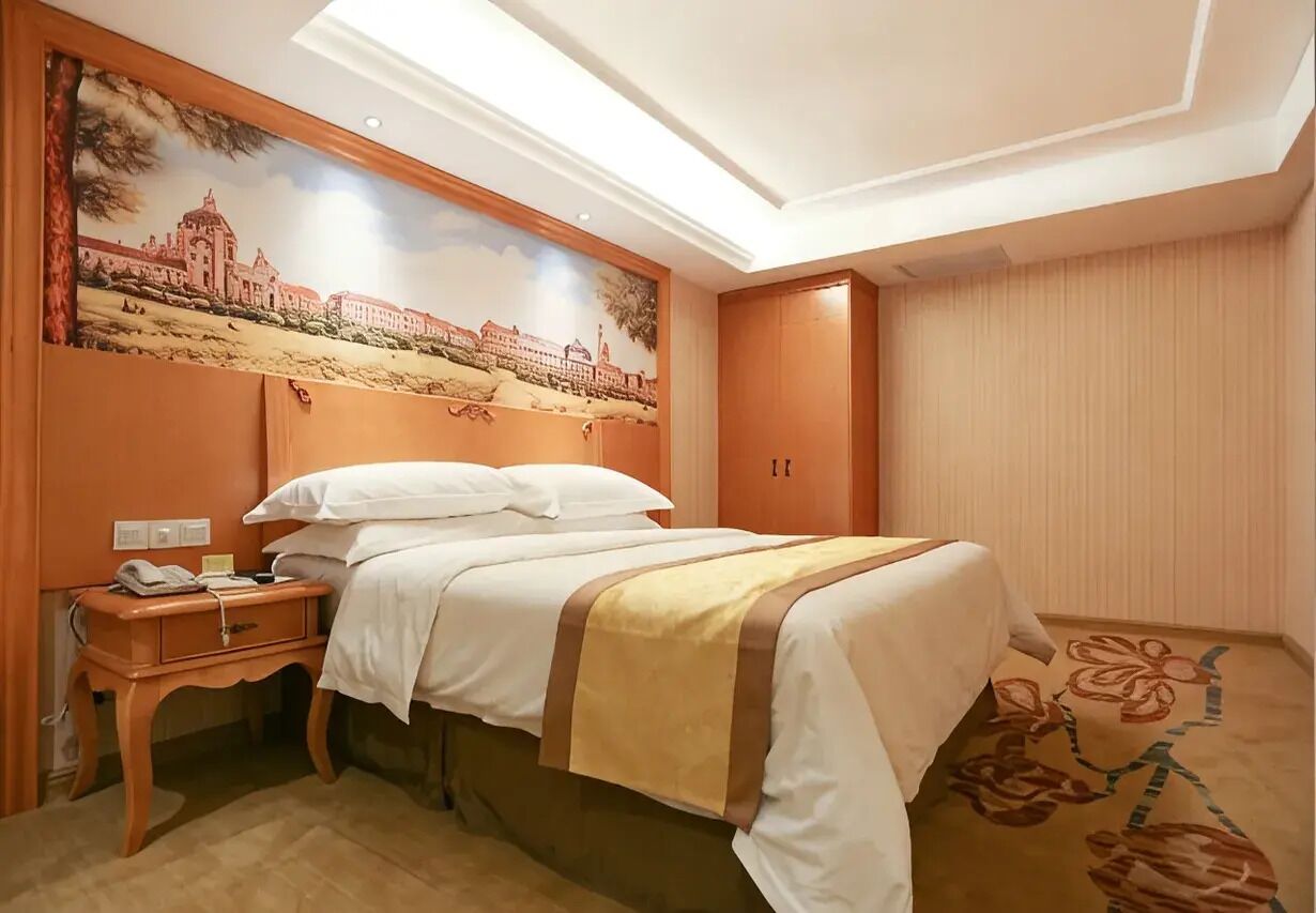 Ein Hotelzimmer mit einem Bett, einem Nachttisch, einem Telefon, einem Wandbild und einer Tür.