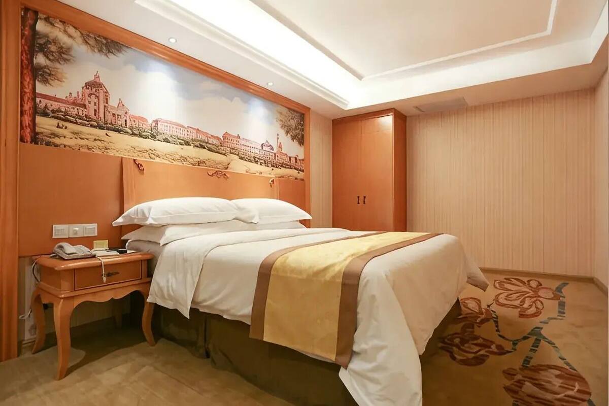 A hotel room with a bed, a nightstand, a telephone, a wall-mounted painting, and a door.