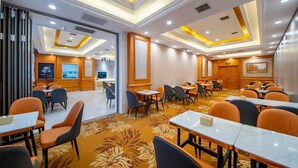 Une salle de conférence d’hôtel équipée de tables et de chaises, d’un espace d’accueil et d’une grande fenêtre.